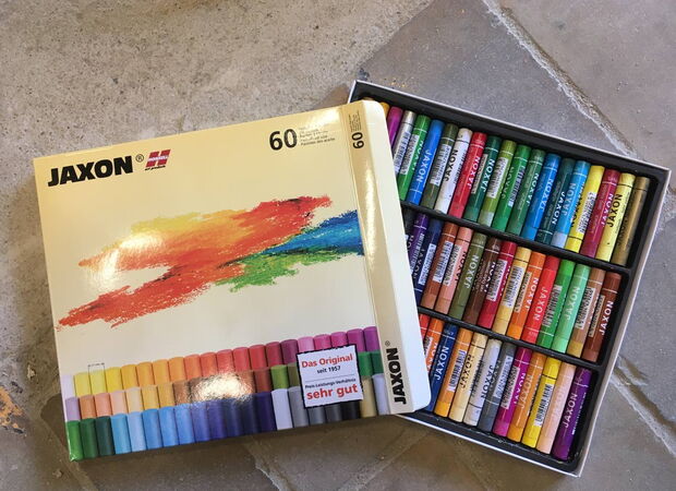 Geöffnete Packung mit 60 farbigen Wachsmalstiften der Marke Jaxon auf einem Steinboden