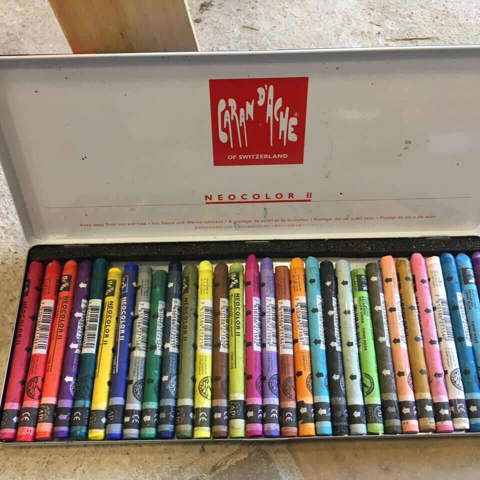 Offene Metalldose mit einer Reihe bunter Wachsmalstifte der Marke Caran d'Ache