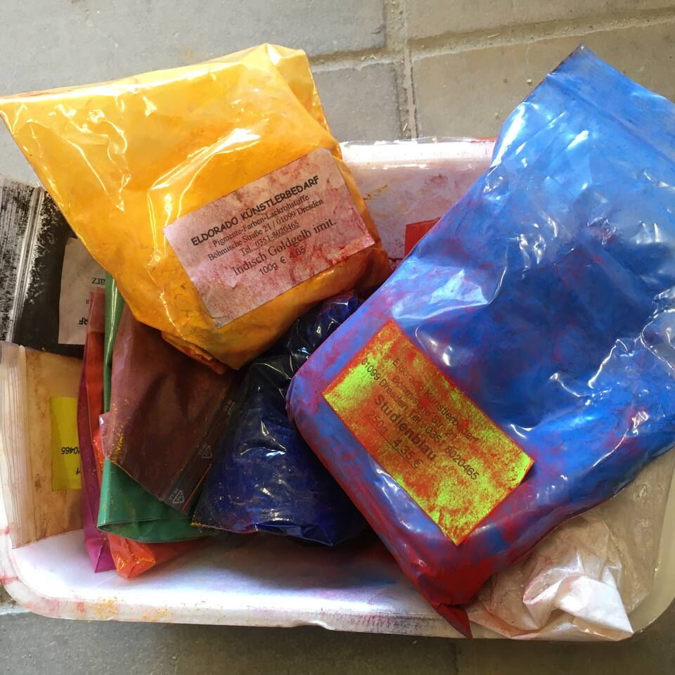 Mehrere bunte Kunststoffbeutel mit Pulver in einer weißen Schale auf einem Steinboden