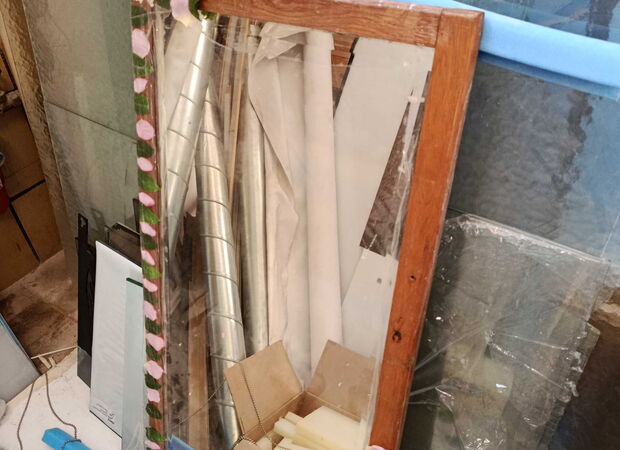 Spiegel mit Holzrahmen lehnt an einer Wand vor verschiedenen Dämmmaterialien und Baumaterialien in einem Lagerraum