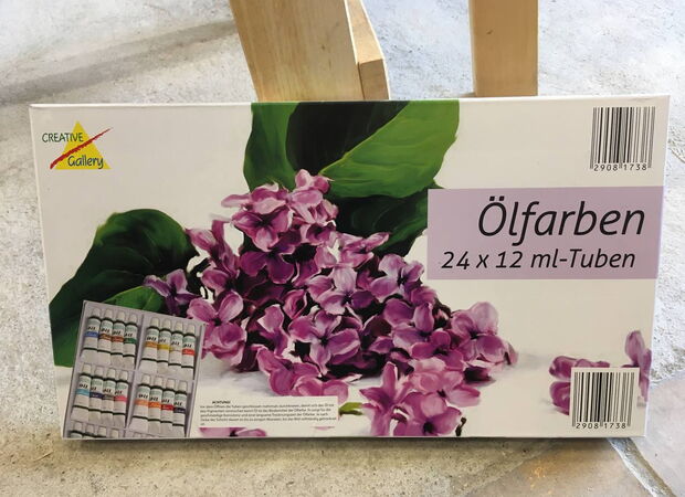Verpackung mit 24 Tuben Ölfarben der Marke Creative Gallery, darauf ein Bild von lila Fliederblüten und grünen Blättern